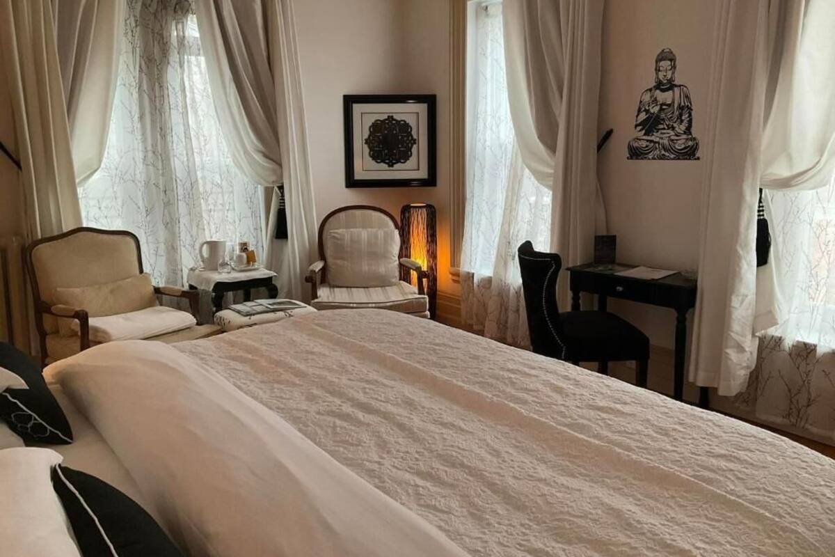 Ein Hotelzimmer mit einem großen Bett, zwei Sesseln, einem Schreibtisch und einer an der Wand befestigten Buddha-Statue.