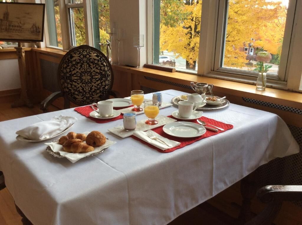 A breakfast table set with plates, cups, and pastries, with a view of autumn trees through the window.