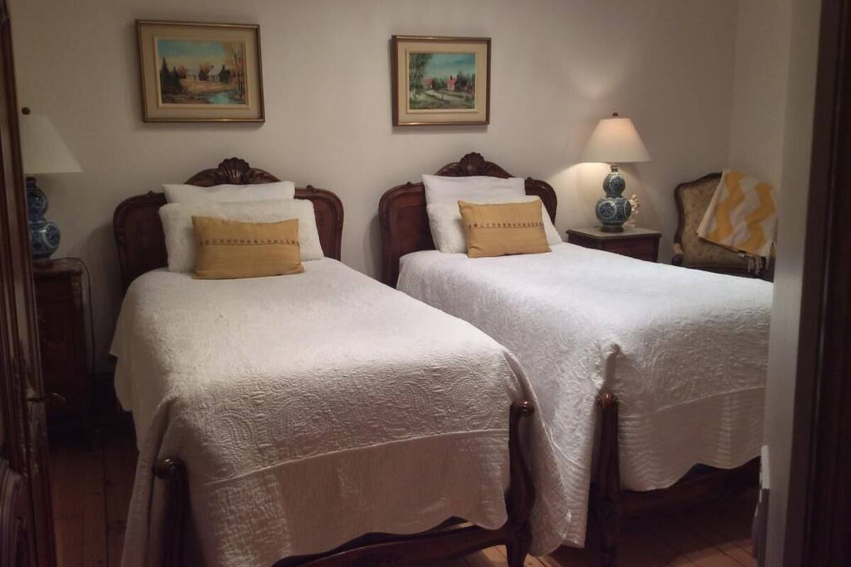 Ein Zimmer mit zwei Betten, jeweils mit weißer Bettdecke und einem Kopfkissen. Darüber an der Wand befinden sich zwei gerahmte Bilder.