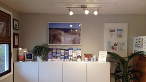 En receptionsdisk med brochurer, et indrammet billede på væggen og en potteplante.