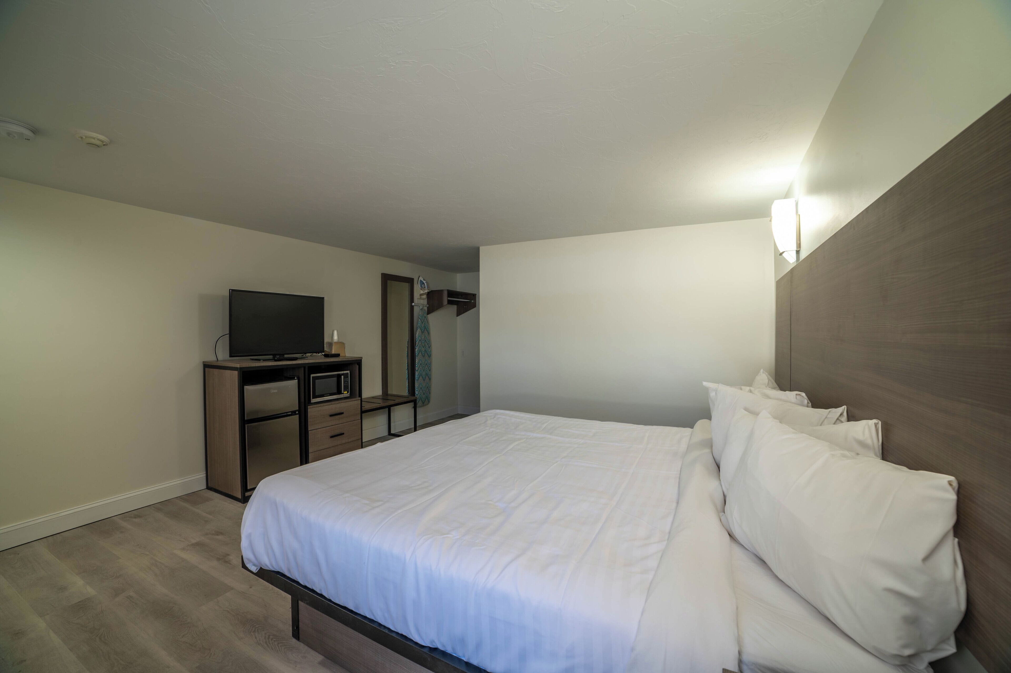 A hotel room with a large bed, a desk with a television, and a mirror.