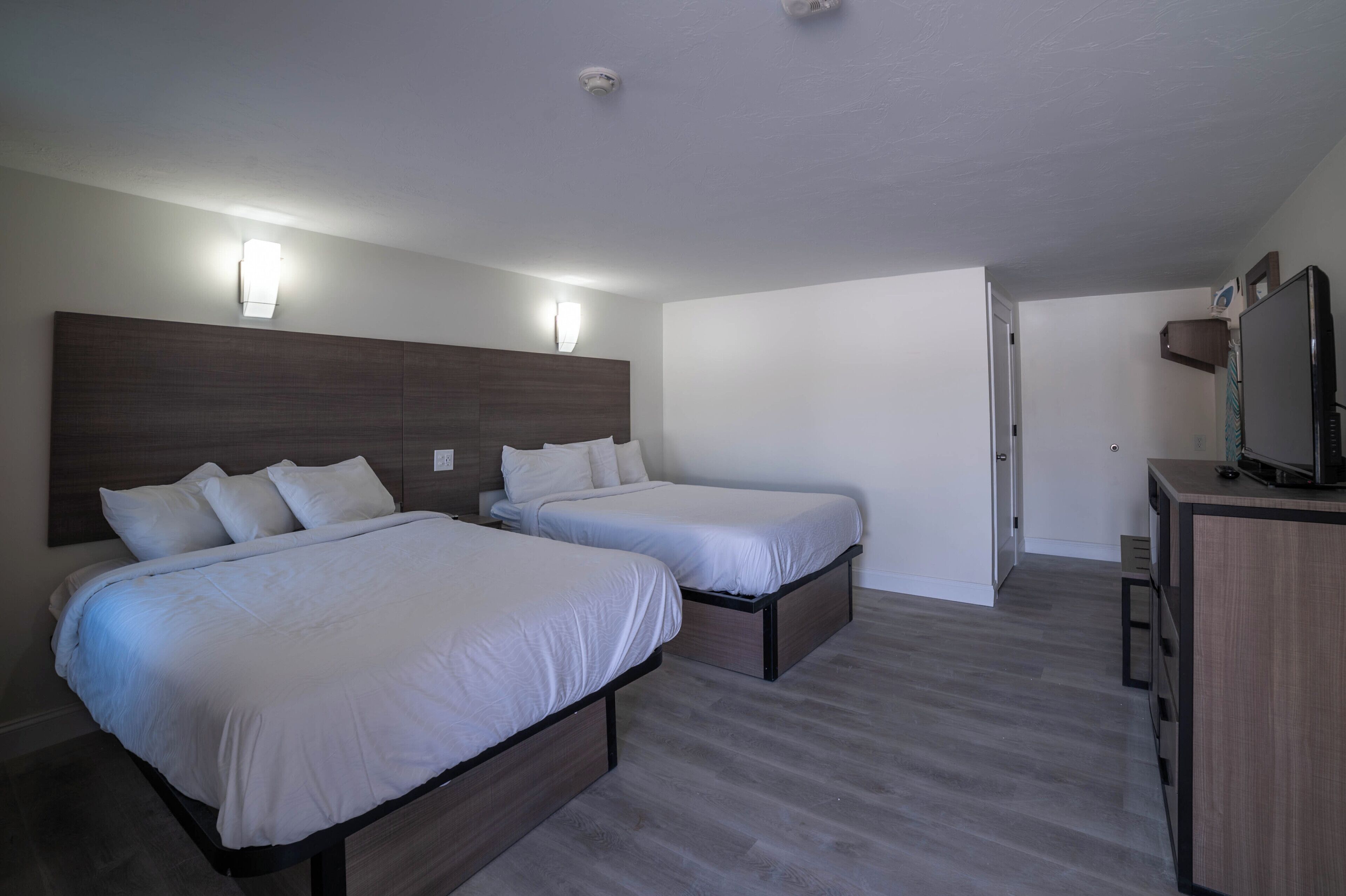 A hotel room with two beds, a desk, and a television.