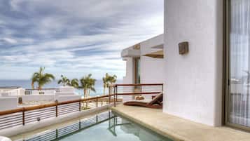 A pool area with a view of the ocean, palm trees, and a modern building with a white exterior.