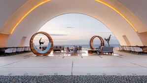 Een modern terras buiten met uitzicht op zee, met ronde houten frames, zitopstellingen en een patroon vloer.