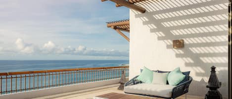 A balcony with a wooden pergola, a white wall, a cushioned sofa with pillows, a small table, and a decorative lantern.