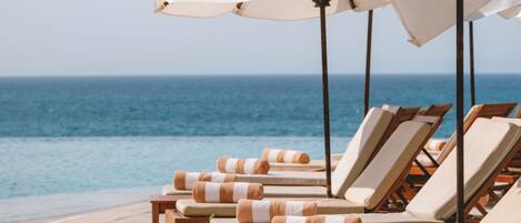 A row of sun loungers with striped towels, white umbrellas, and a view of the ocean.