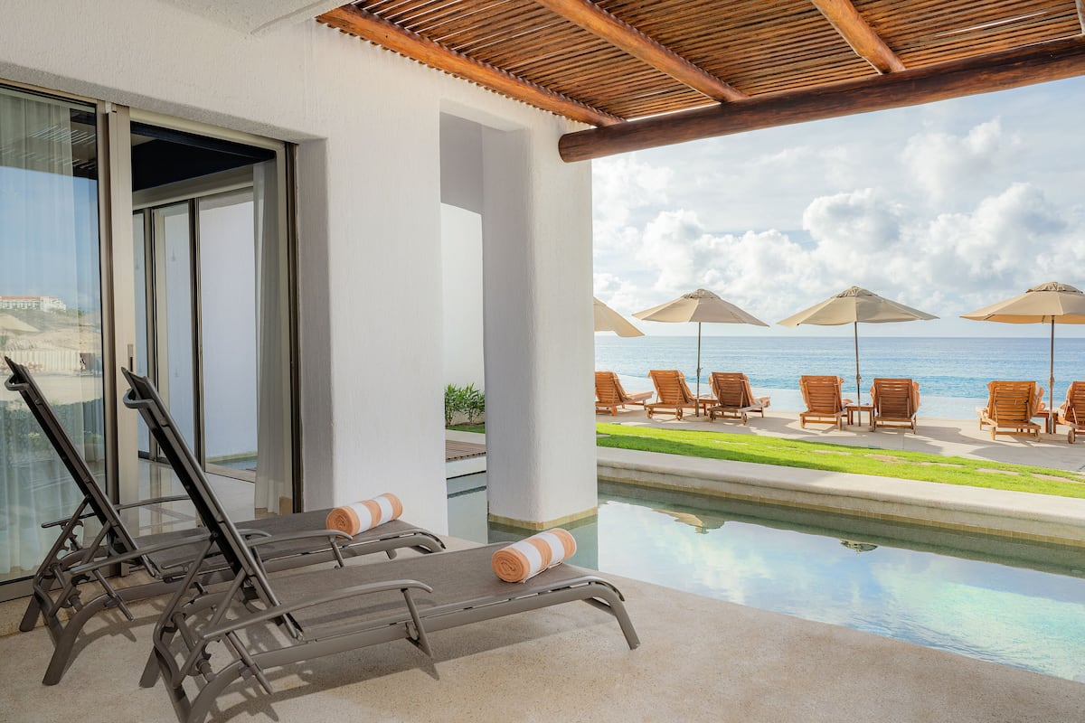 Ein Poolbereich mit Liegestühlen und Sonnenschirmen mit Blick auf ein klares, blaues Meer.