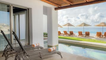 A poolside area with lounge chairs and umbrellas, overlooking a clear blue sea.