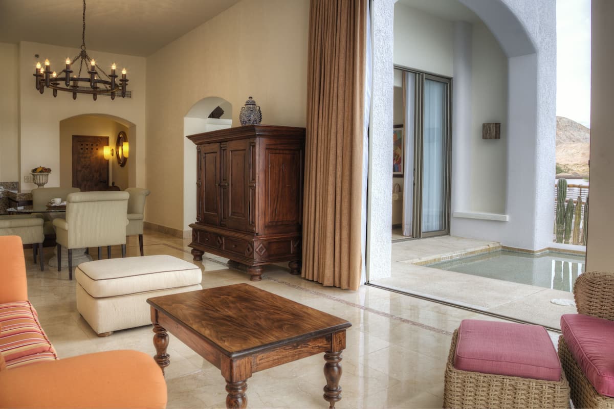 Ein geräumiges Wohnzimmer mit einer Chandelieber, einem Holzschrank und Blick auf einen Pool durch eine Glastür.