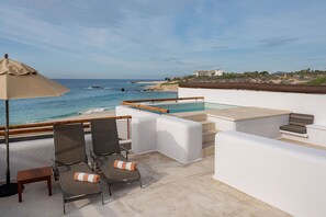 Un espace piscine aménagé sur le toit, offrant une vue sur l’océan, avec un fauteuil de relaxation, une petite table et un parasol beige.
