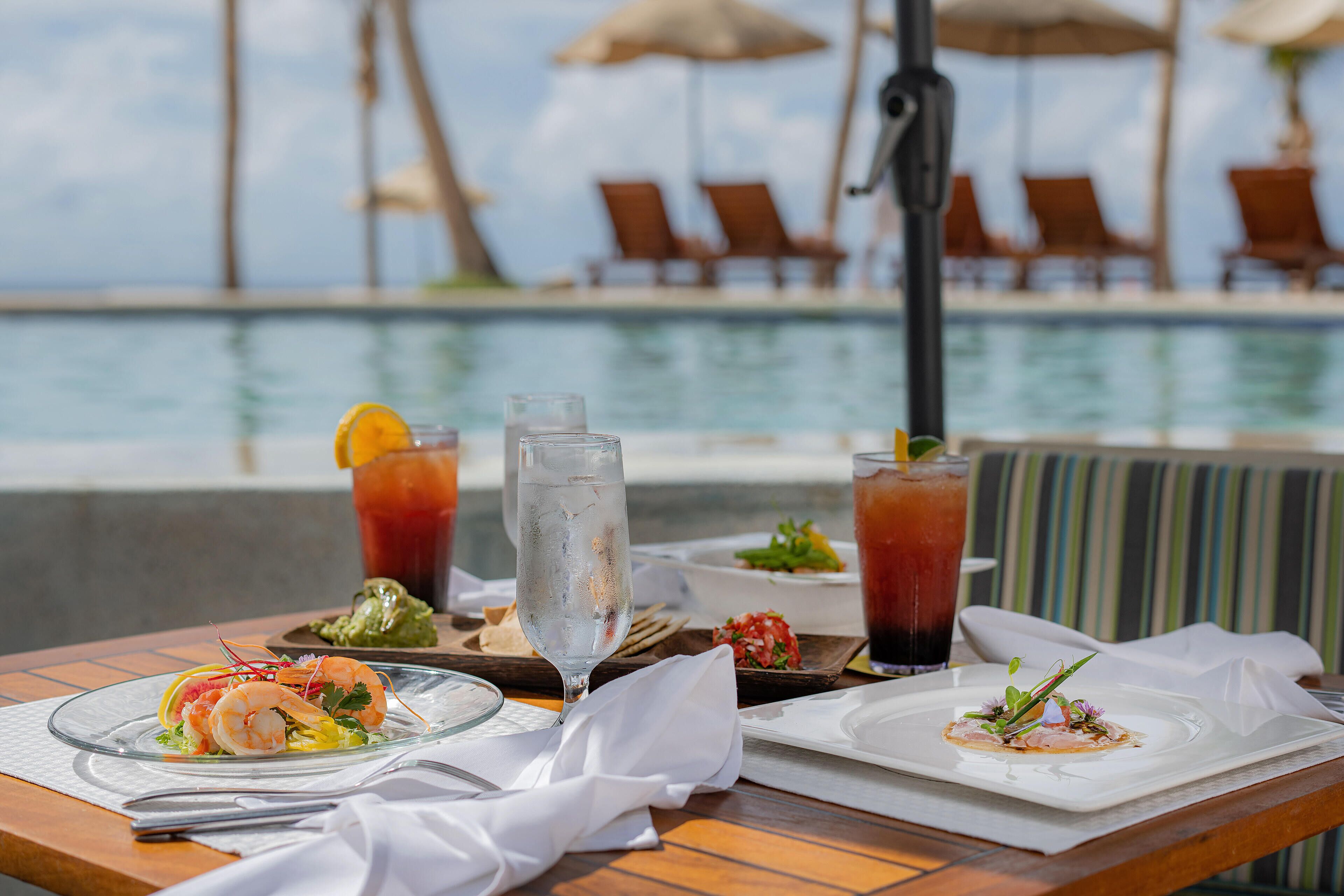 A dining table with seafood dishes, drinks, and a view of a pool and lounge chairs.