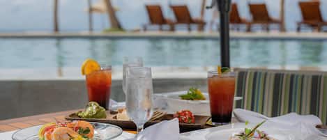 A dining table with seafood dishes, drinks, and a view of a pool and lounge chairs.