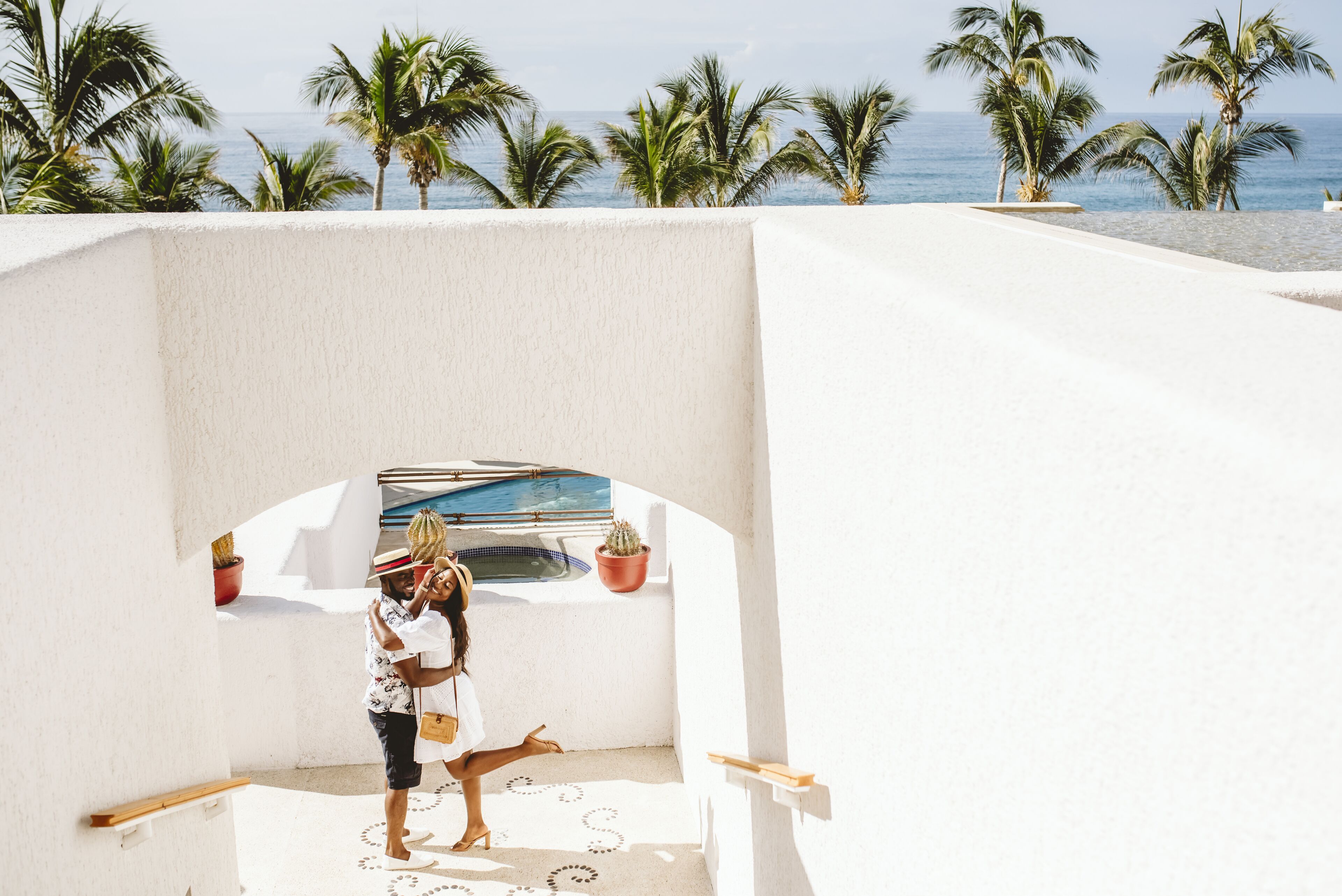 A white-walled structure with a pool, palm trees, and a view of the sea.