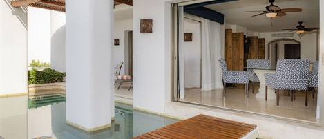 Un área de piscina con terraza de madera, zona de comedor con sillas estampadas y un ventilador de techo.