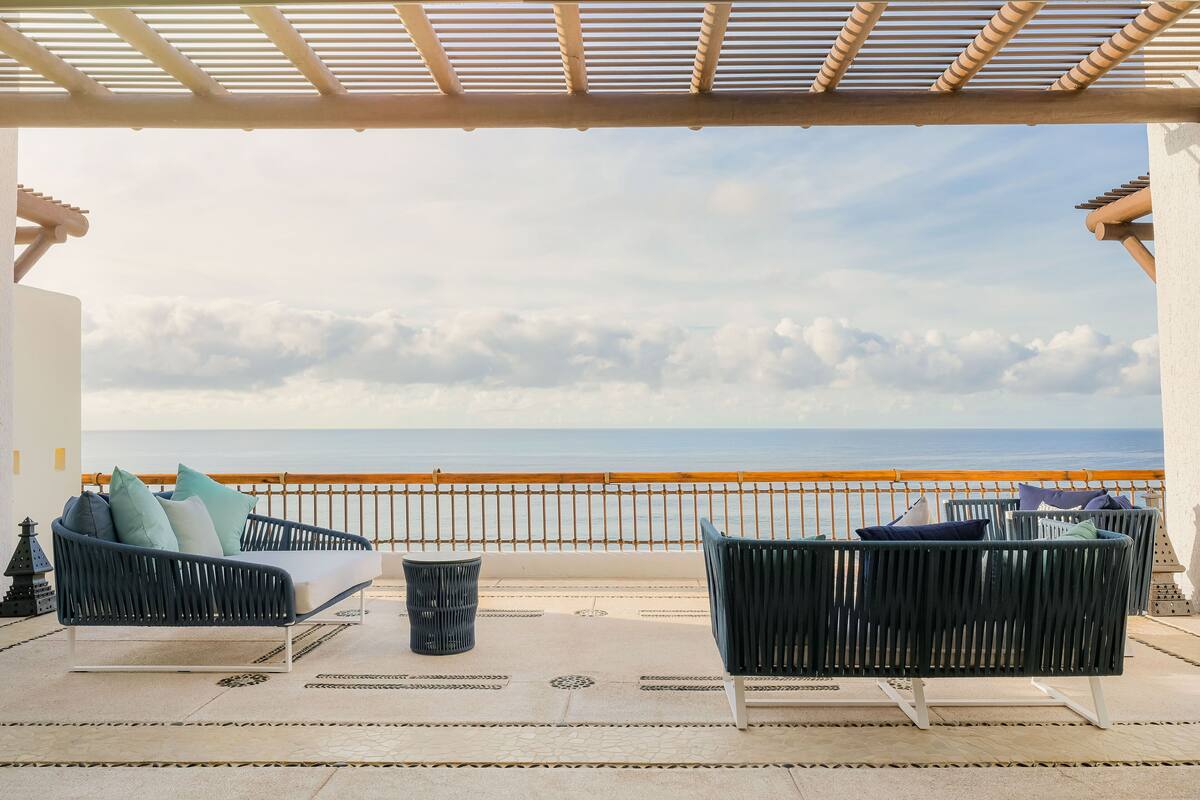 Ein Balkon mit zwei schwarzen Korbssesseln, einem kleinen Mülleimer und einem Geländer mit Blick auf das Meer.