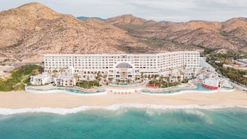 Un grand complexe hôtelier doté de plusieurs piscines, d’une plage et d’un paysage montagneux en arrière-plan.