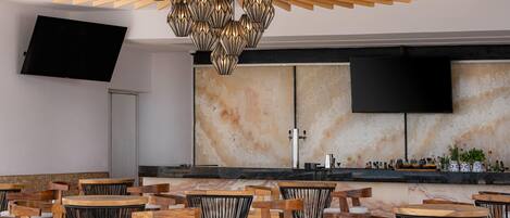 Un bar moderno con sillas y mesas de madera, una lámpara de araña grande y un televisor de pantalla plana montado en la pared.