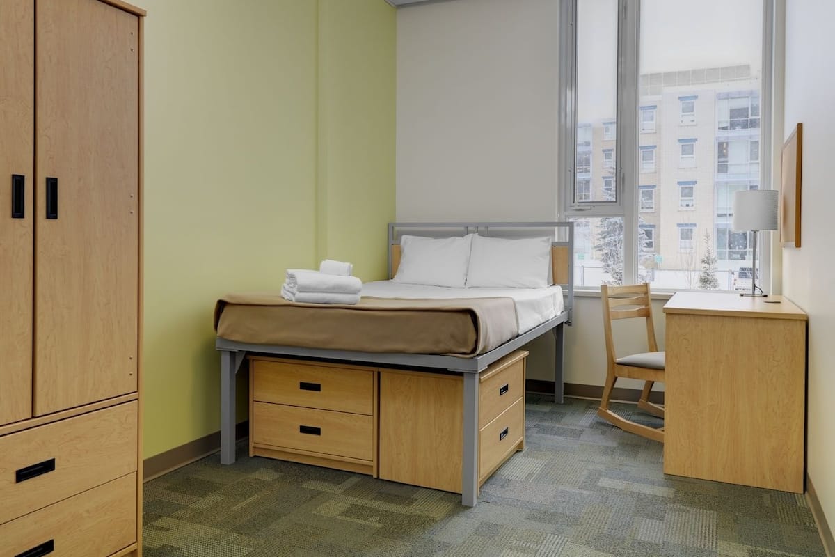 A bedroom with a bed, a desk, a chair, and a wardrobe.