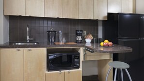 A modern kitchen with wooden cabinets, a black refrigerator, a microwave, and a coffee maker. - University of Calgary - Seasonal Residence (Calgary)