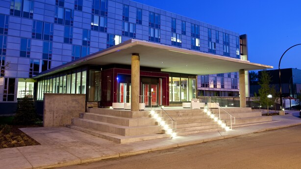 A modern hotel with a glass facade, a covered entrance, and a staircase leading to the lobby. - University of Calgary - Seasonal Residence (Calgary)