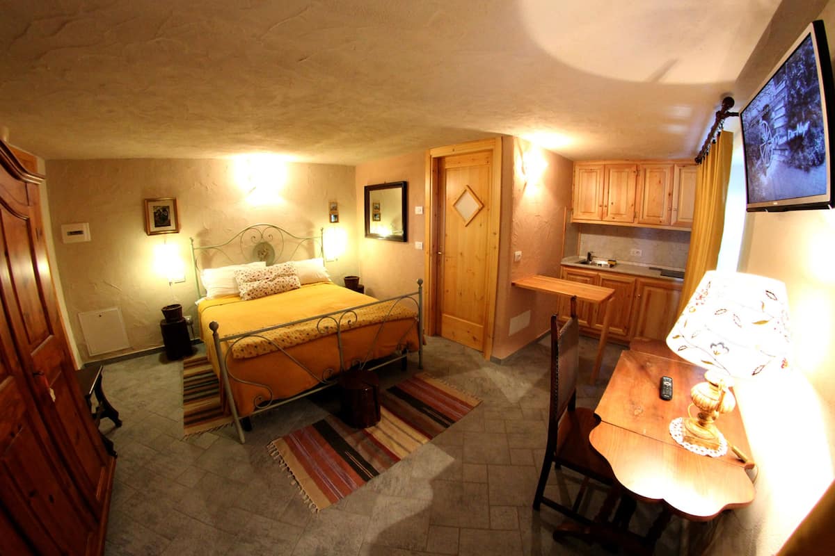 A bedroom with a bed, bedside lamps, a wooden door, and a small kitchenette.
