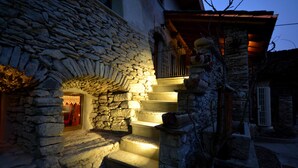 Una escalera de piedra conduce a una puerta con cortina roja, una pared de piedra y un pequeño balcón con barandilla.