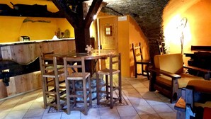 Un interior rústico con una mesa y sillas de madera, un piano y una pared de piedra.