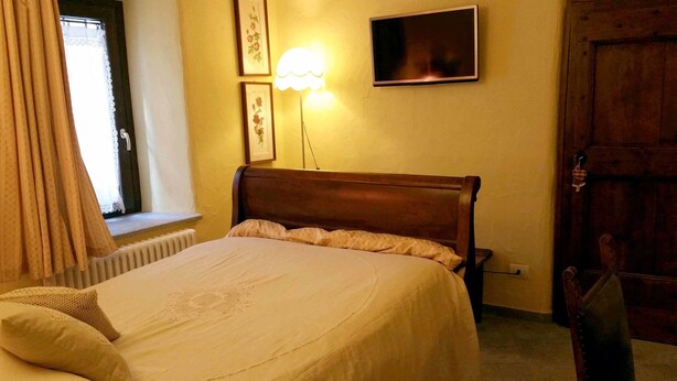 A bedroom with a wooden bed, a bedside lamp, a framed picture, and a door. - Maison Du-Noyer (Aosta)