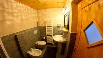A compact bathroom with a toilet, bidet, sink, and a wooden door with a window.