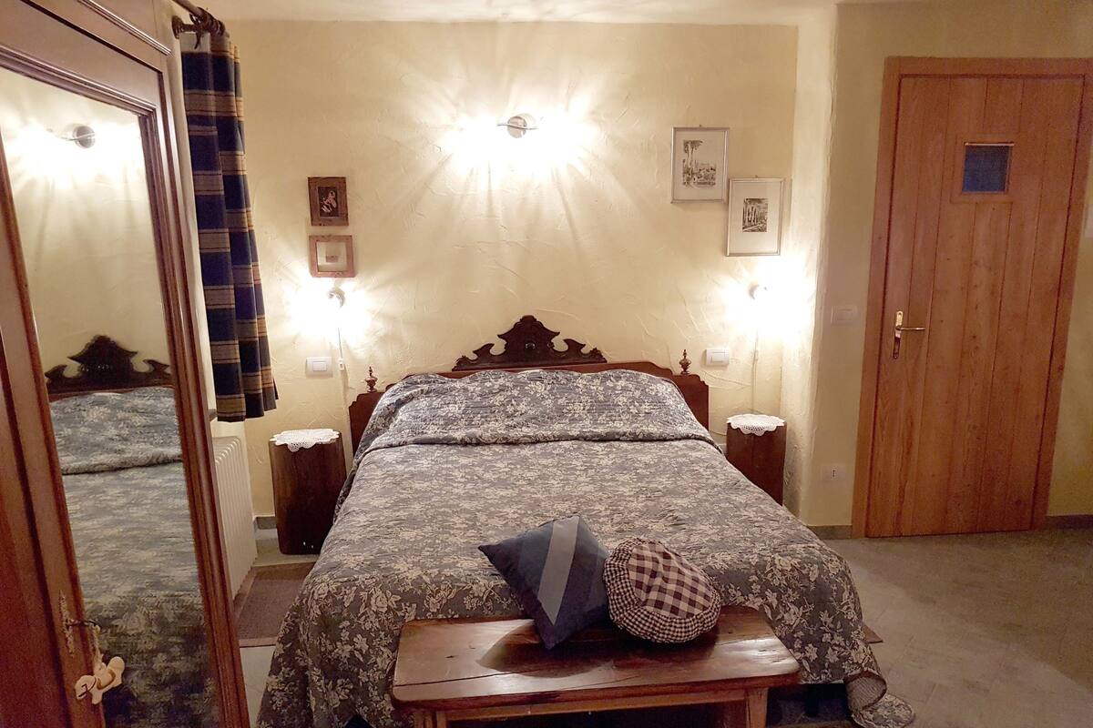 A bedroom with a bed, bedside tables, a wooden door, and a mirror.