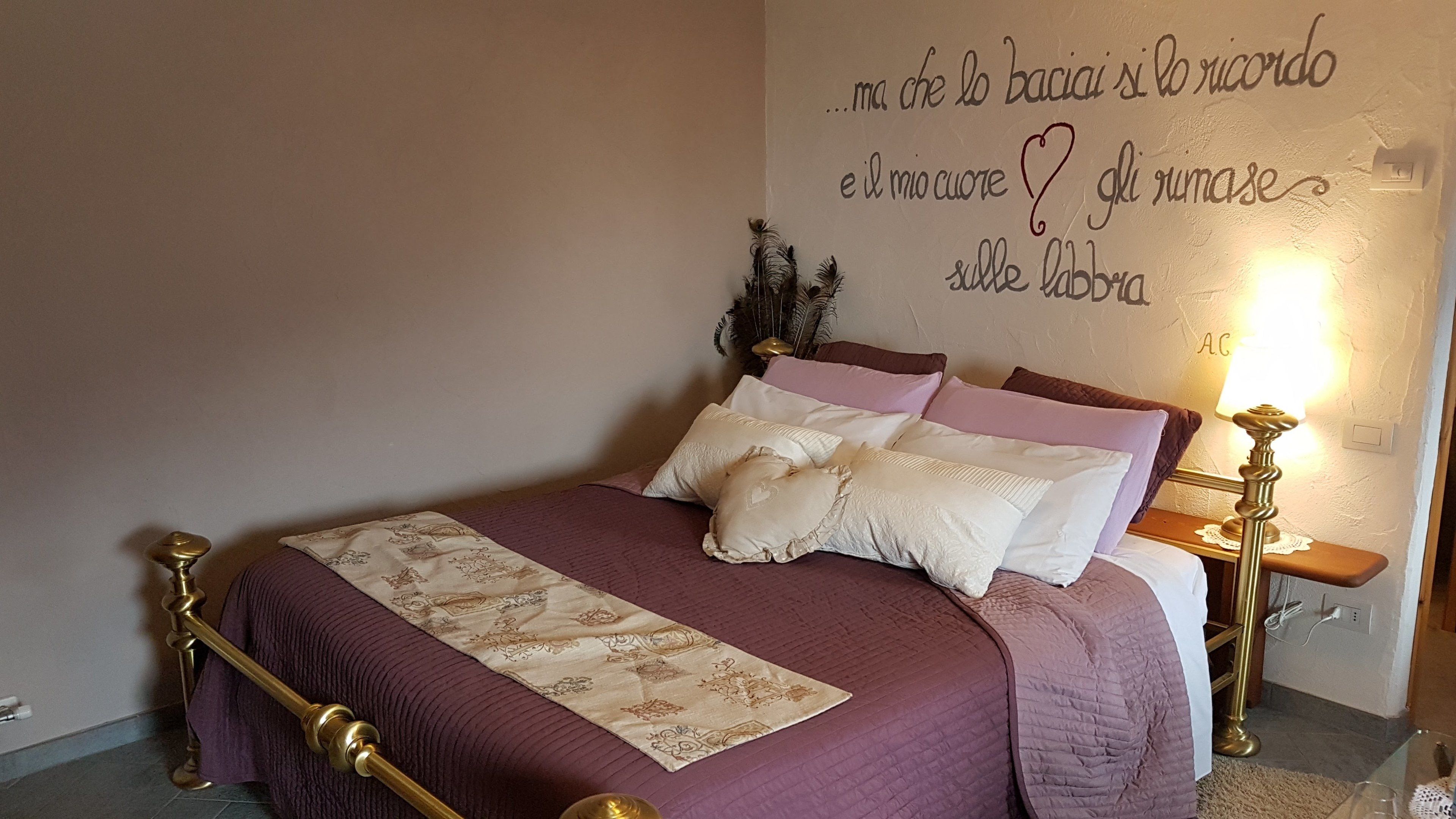 Un lit bien fait, avec une couvre-lit à motifs et des oreillers, un mur orné d’une inscription décorative et une lampe de chevet.