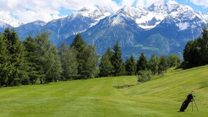 Un campo de golf con montañas nevadas y un bosque denso al fondo.