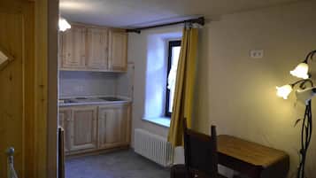 Una piccola cucina con mobili in legno, una finestra con tenda gialla e un tavolo con sedie.
