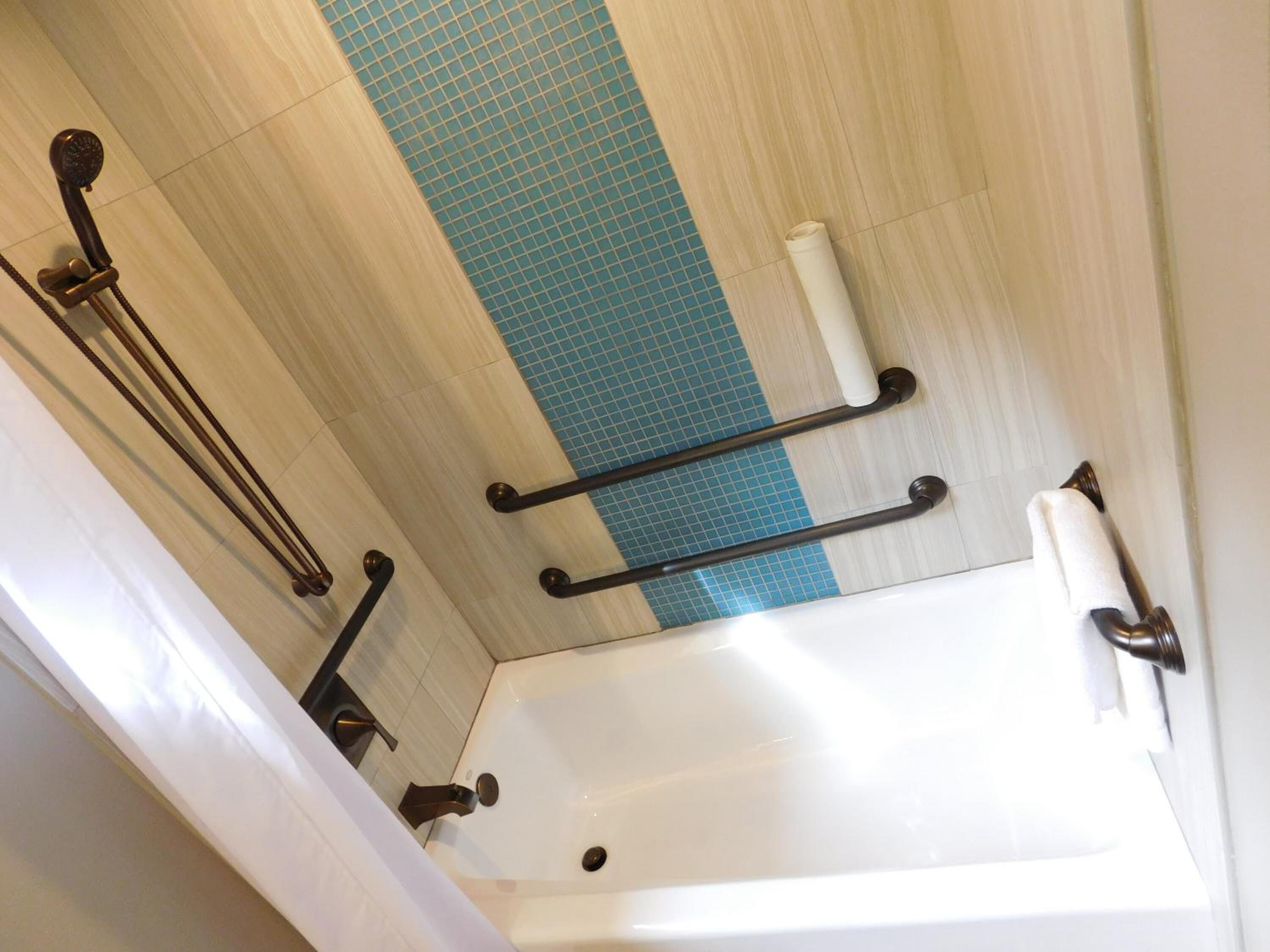 A bathroom with a bathtub, grab bars, and a towel rack.