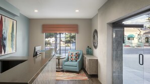 A reception area with a modern counter, a seating area with a chair and a rug, a large window with blinds, and a door leading outside. - Wave Street Inn (Monterey)