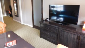 A hotel room with a large flat-screen TV on a dark wooden cabinet, a desk with a chair, and a sliding door closet. - Wave Street Inn (Monterey)