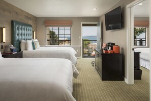 A hotel room with two beds, a TV, a balcony with a view, and a desk with a coffee machine.