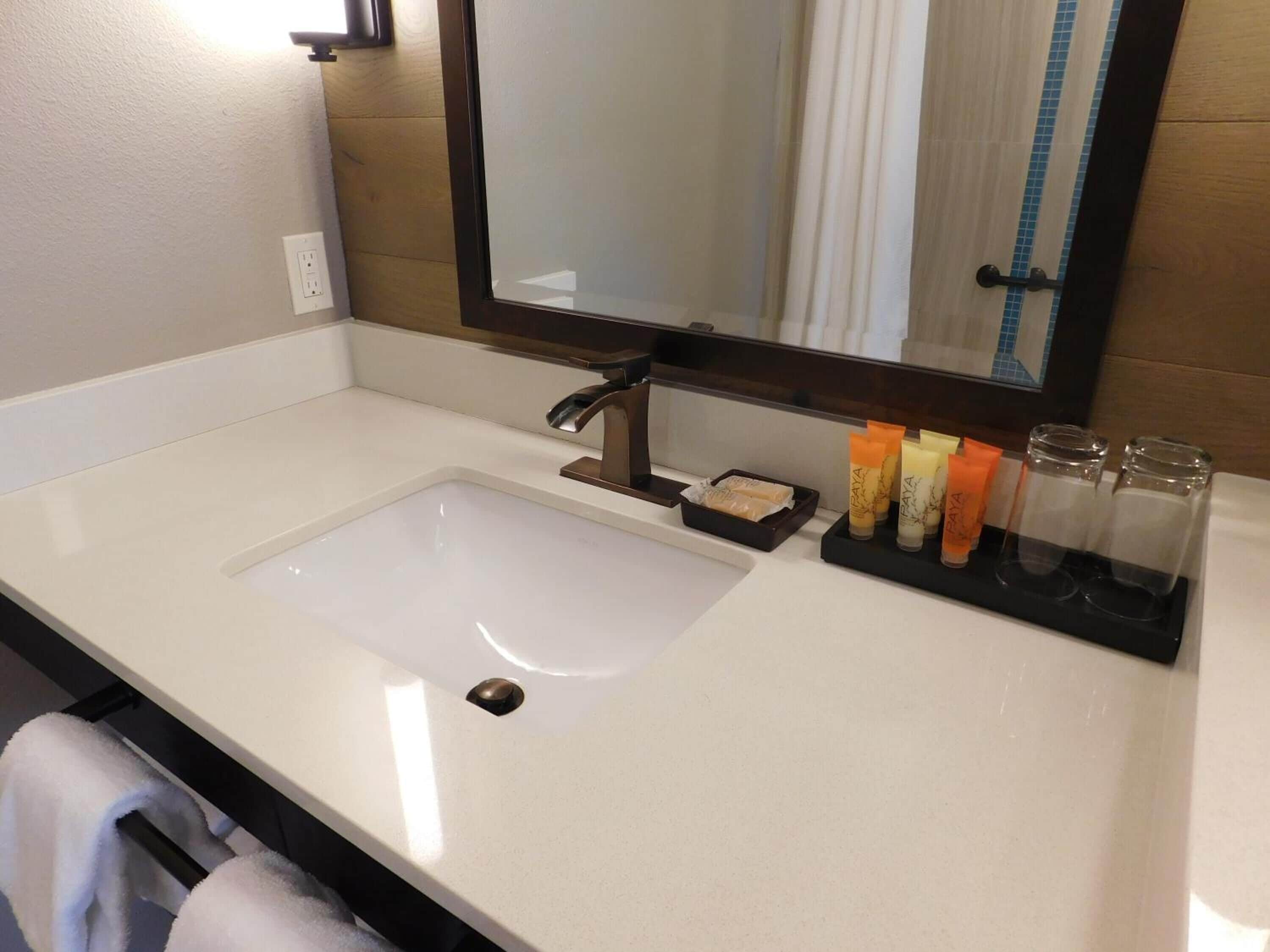 A bathroom with a white sink, a mirror, and toiletries on the counter.