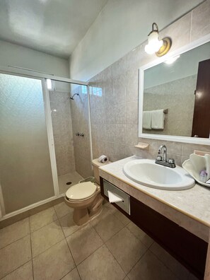 Un baño moderno con ducha de vidrio, inodoro, lavamanos con espejo y un perchero para toallas.