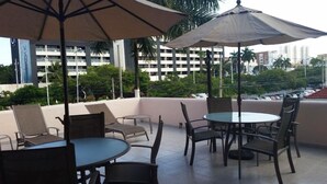 An outdoor seating area with tables and chairs, umbrellas, and a view of a cityscape with buildings and palm trees. - Hotel Handall Cancun (Cancun)