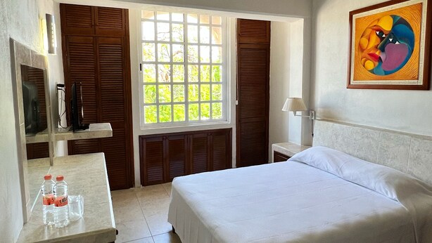 A hotel room with a bed, a desk with a mirror, a window with shutters, and a painting on the wall. - Hotel Handall Cancun (Cancun)