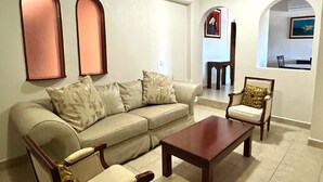 A living room with a sofa, two armchairs, a coffee table, and a dining area with a chair and table. - Hotel Handall Cancun (Cancun)