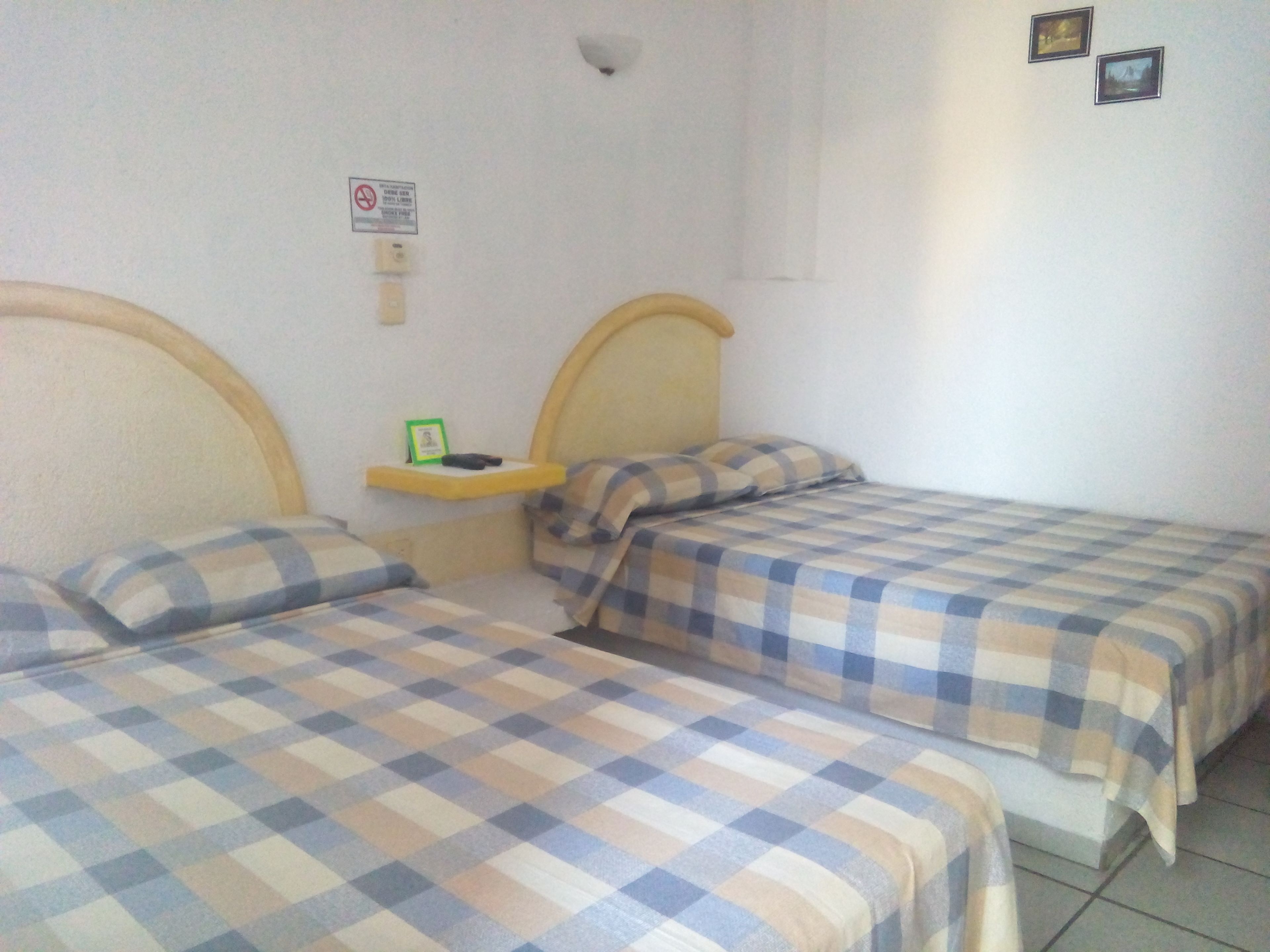 Ein Zimmer mit zwei Betten, jedes mit einer karierten Bettdecke. Es gibt ein kleines Regal mit einem gerahmten Foto und einem kleinen Gegenstand darauf.
