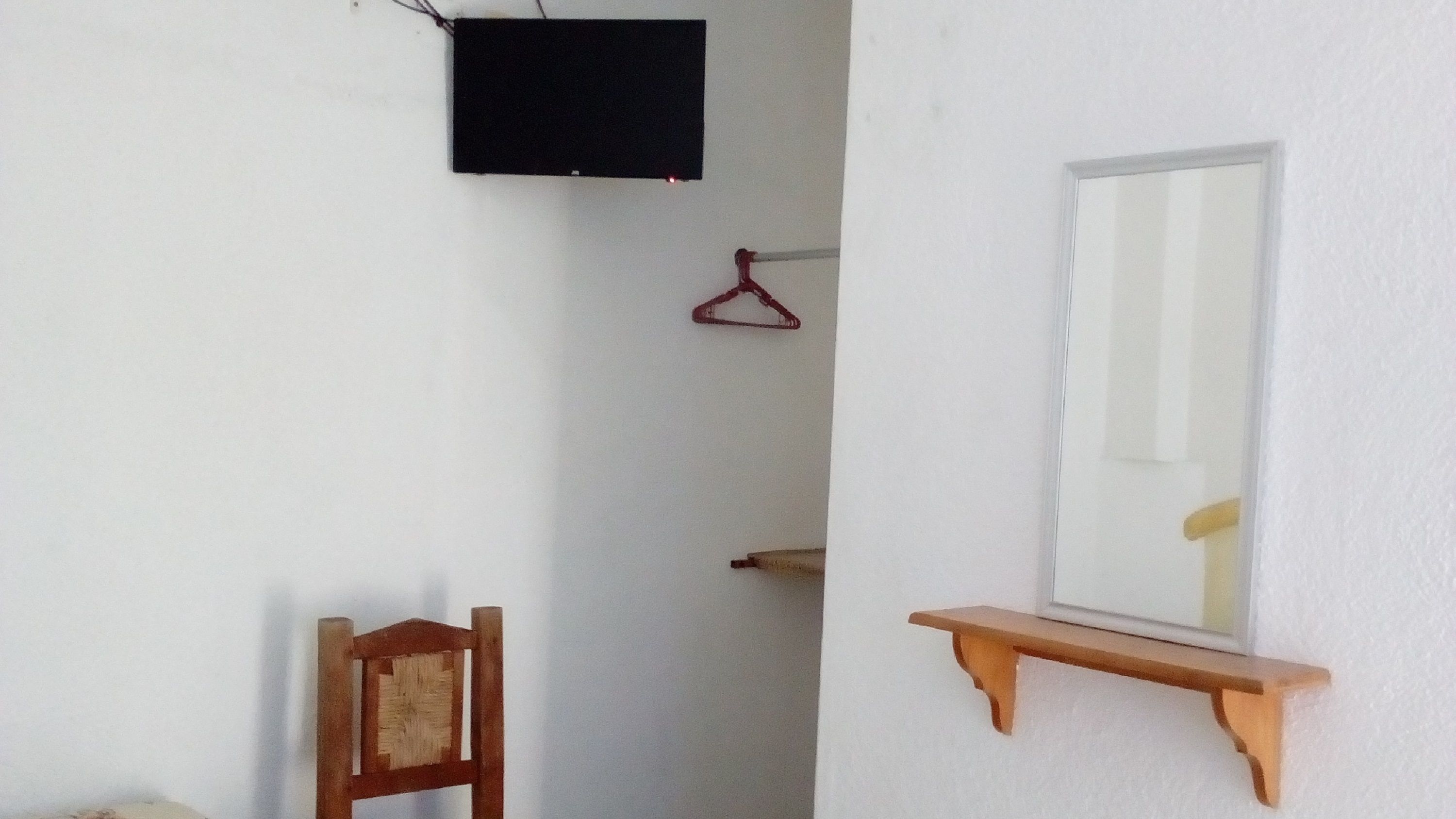Una habitación con una silla de madera, un estante de madera con un espejo, un perchero rojo y un televisor montado en la pared.