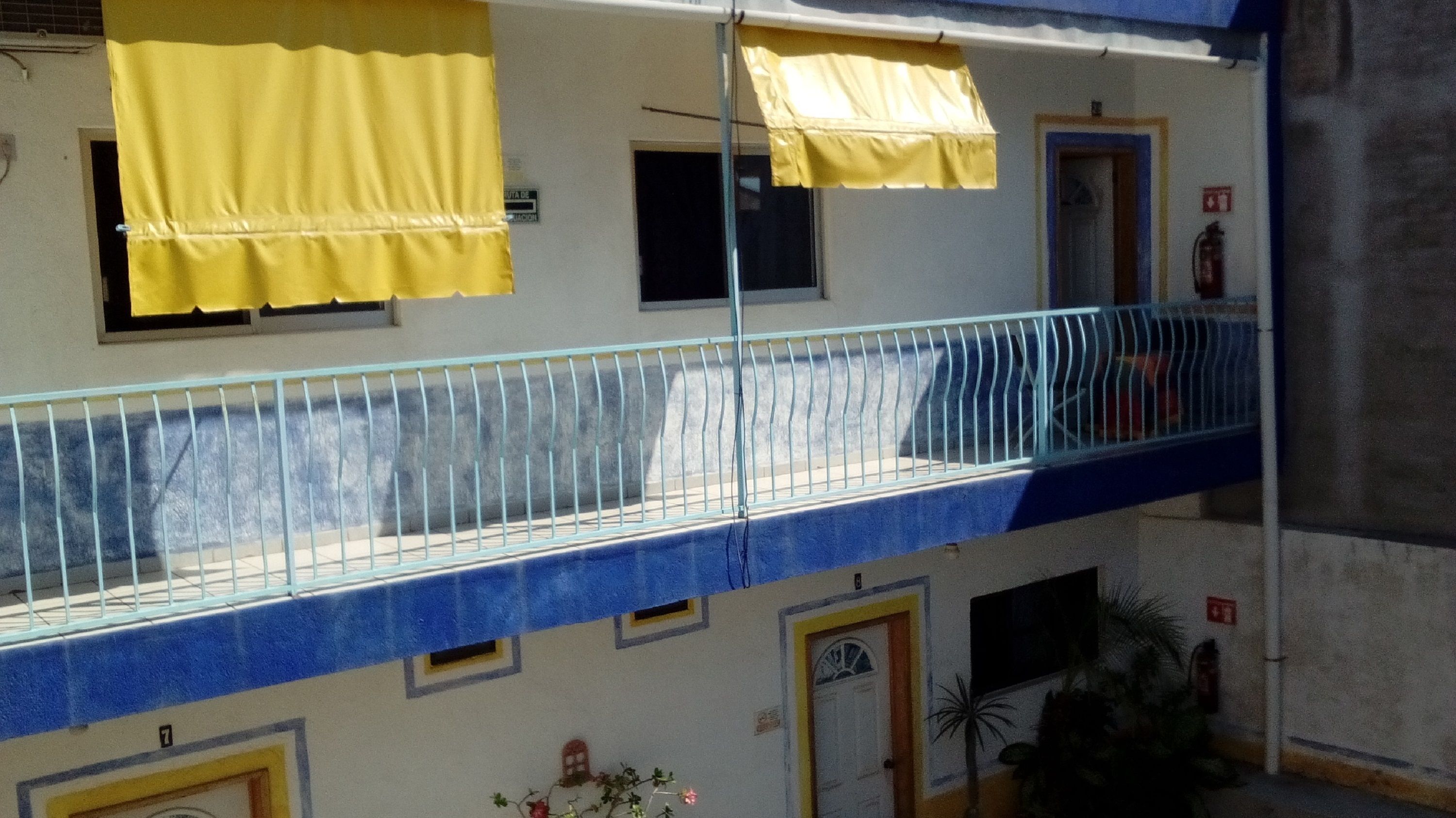 A multi-story building with balconies, yellow awnings, and a blue railing.