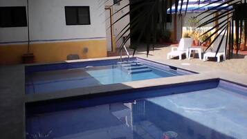 Una piscina con bordeado de baldosas, rodeada de plantas en macetas y mobiliario de exterior.