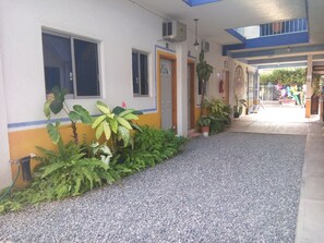 Un bâtiment avec un chemin de gravier menant à une porte, entouré de plantes en pot et dont la façade est bleue et blanche.