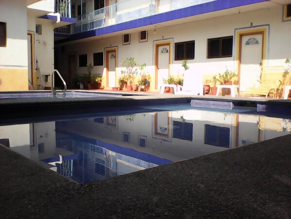 Une piscine dont l’eau est si claire qu’elle reflète l’environnement, entourée de plantes en pot et de portes.
