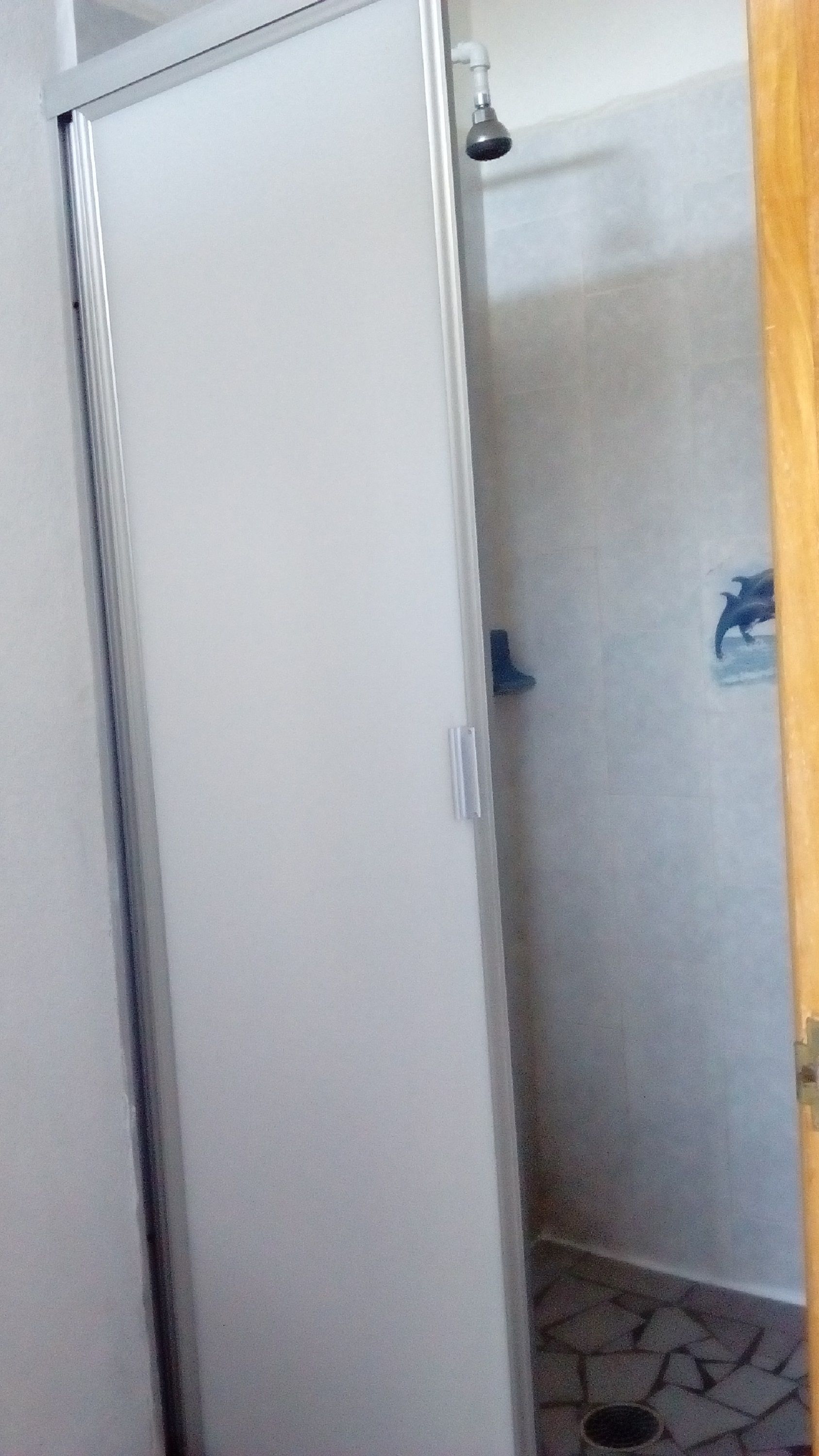 Un baño con ducha, suelo de baldosas y una puerta.