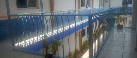 Um edifício com guarda-corpo azul, plantas em vasos e pisos ladrilhados.
